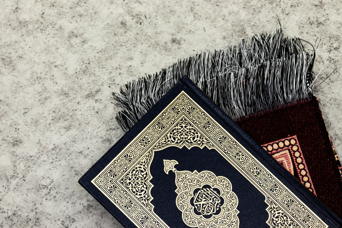 Holy Quran with Arabic calligraphy meaning of Al Quran and prayer mat
